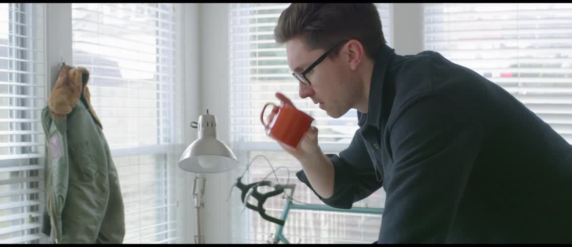 A man looking at a typewriter and drinking from a mug