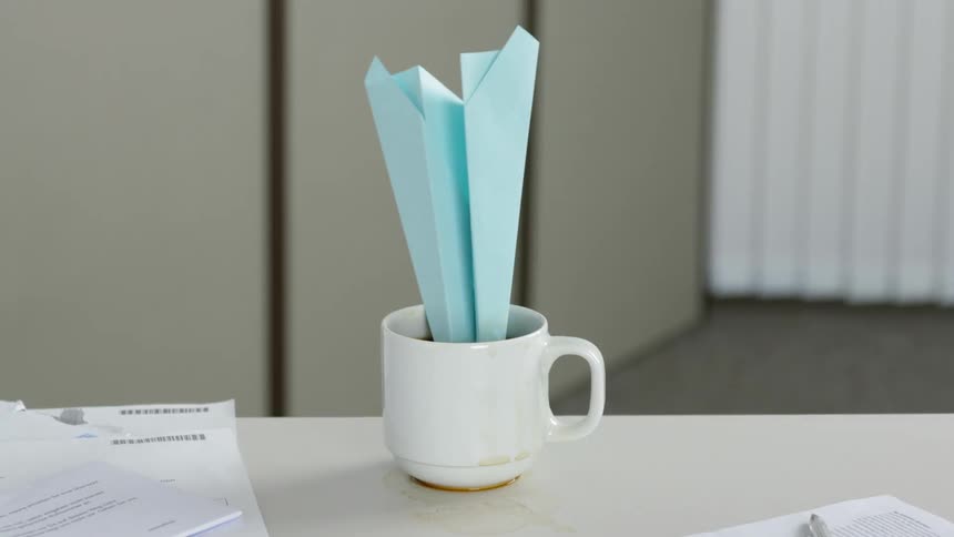A paper airplane landing nose first in a mug of coffee