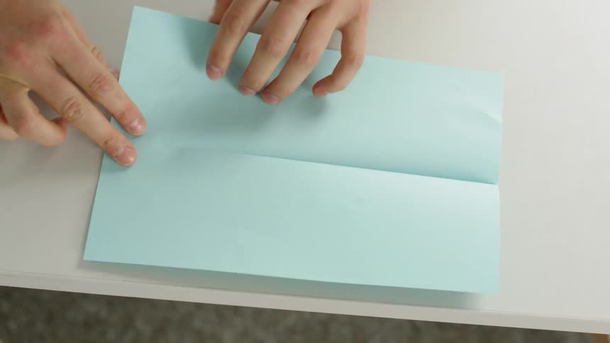 A person folding a piece of blue paper on a white table