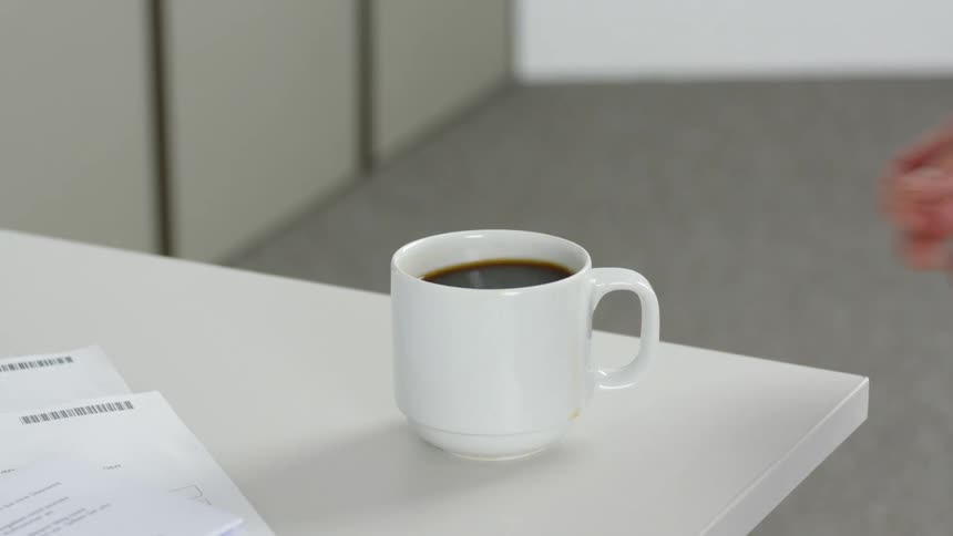 Person sets coffee mug with coffee on table, then picks it up