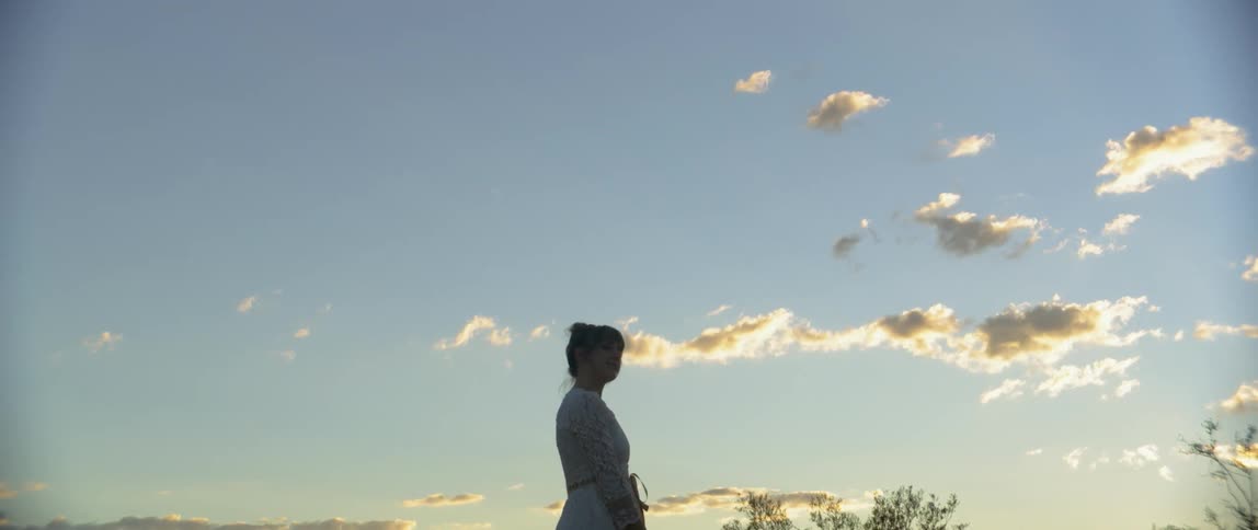 A woman spins and dances in a rural field at sunset