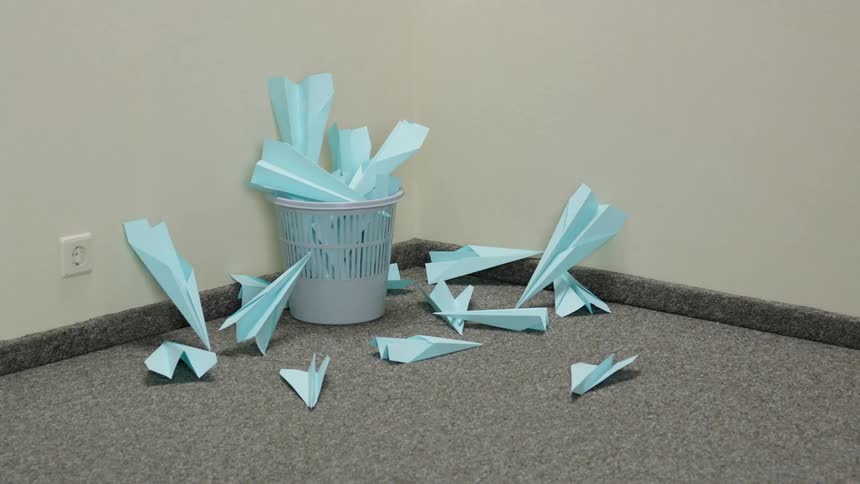 Paper airplanes litter the ground around a wastebasket