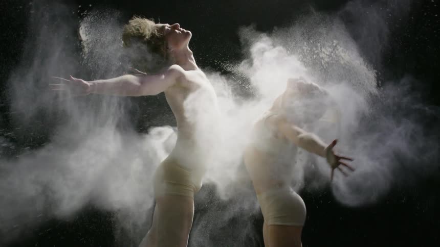 Male and female dancer jumping with powder being thrown on them