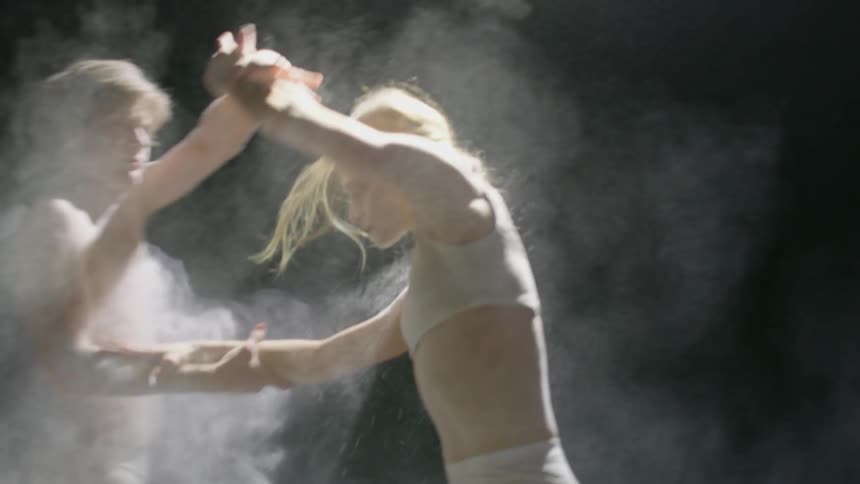 Two dancers perform a sequence together as a smoke machine renders them in mist