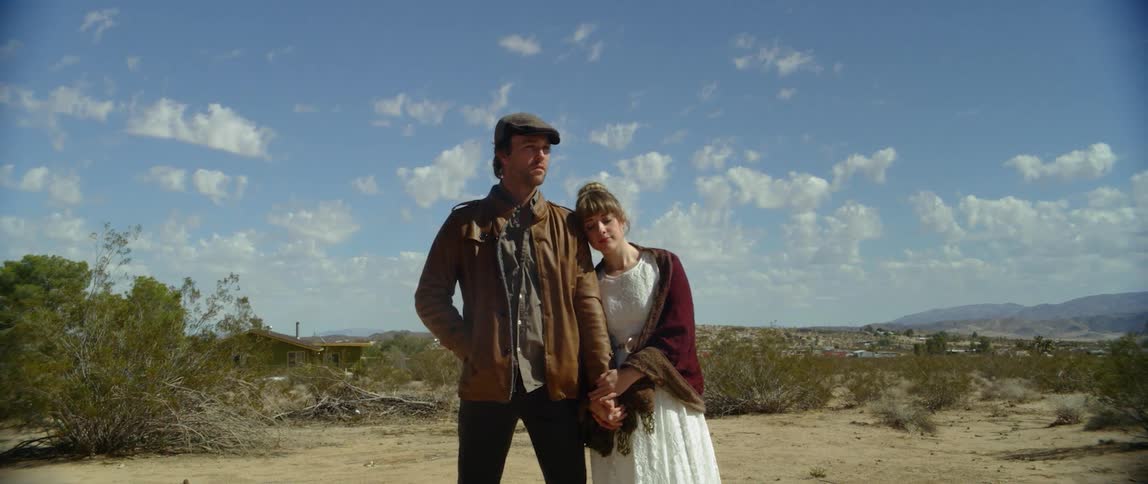 Man and woman wearing homespun clothing standing in a field of dirt