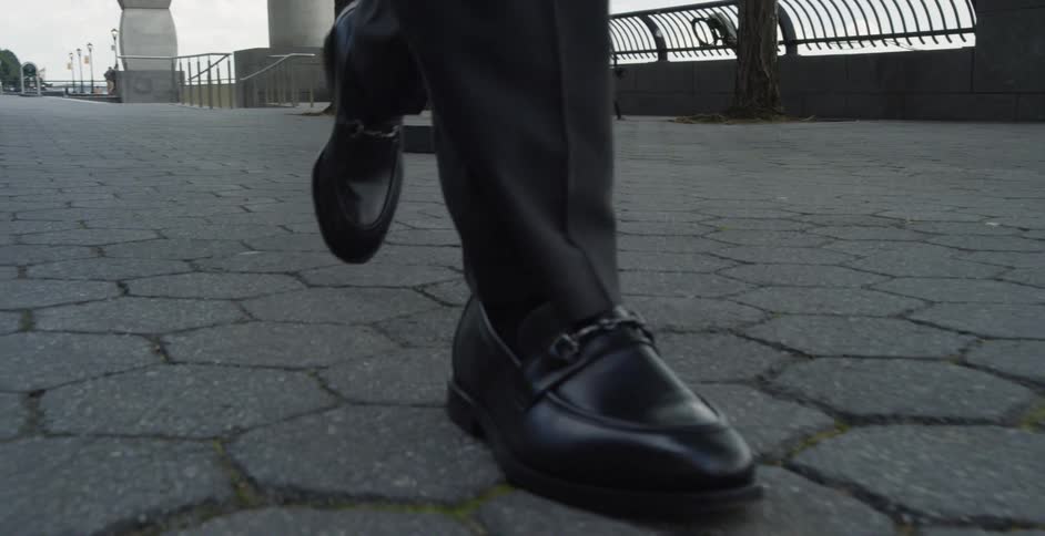 A man in black dress shoes socks and pants walking on a boardwalk