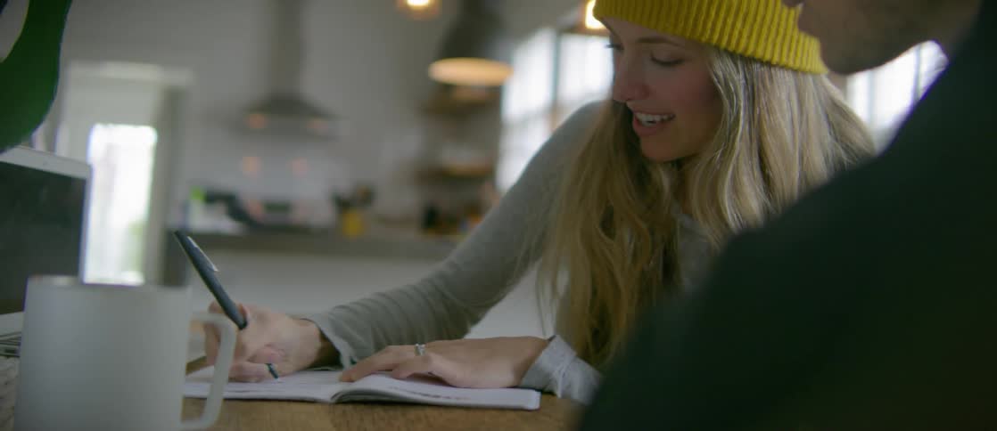 A woman with a bright yellow hat writes things down while talking to a man