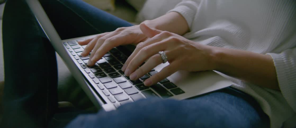 A woman sitting down on the floor typing on a laptop between her legs