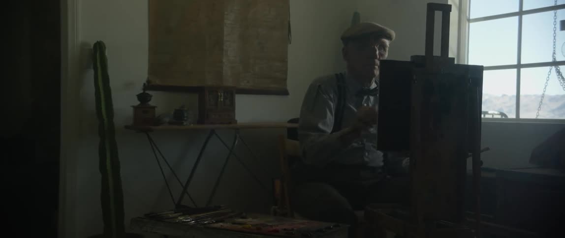 An old man wearing a cap applies paint to a canvas