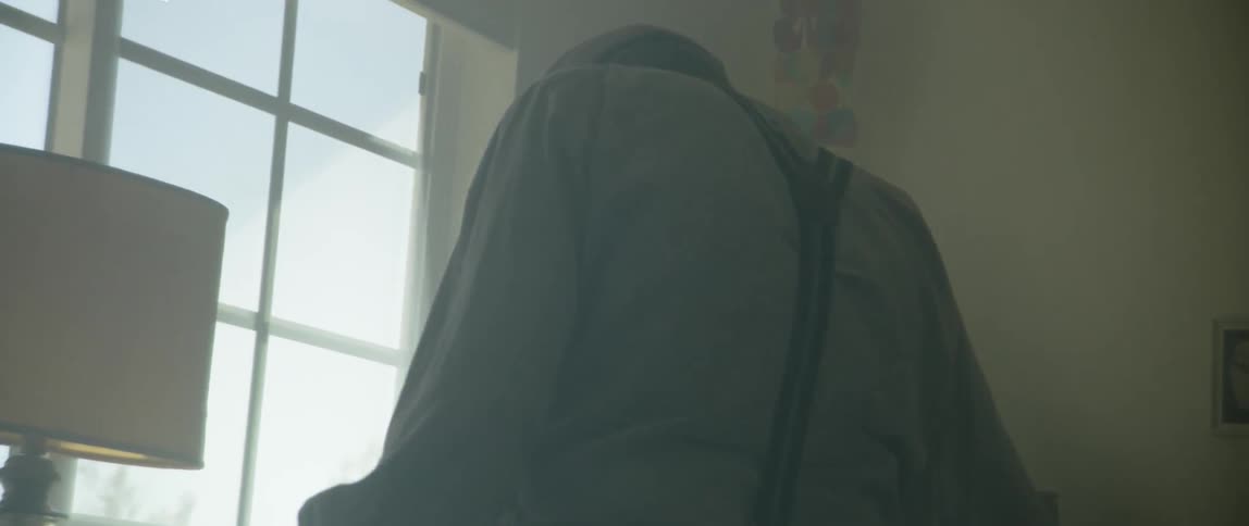 A man with suspenders and a hat walking towards a desk and sitting down