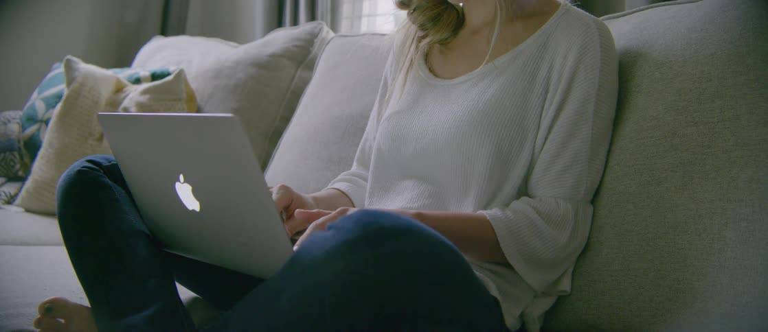 A woman sitting on a couch and typing on a laptop
