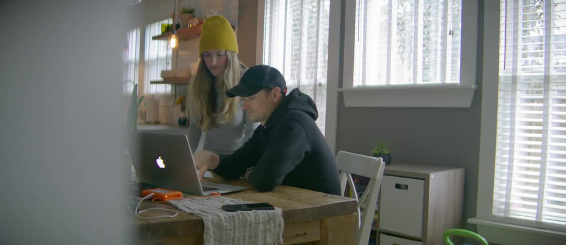 A young woman writes something on a piece of paper and a young man types what she wrote into an apple laptop