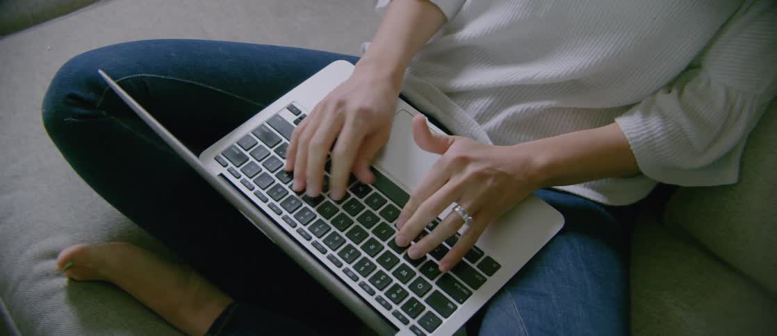 A woman typing on a laptop sitting on her crossed legs