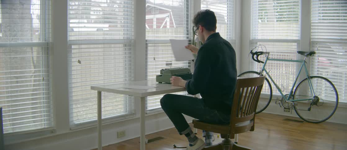 A young man in jeans and glasses completes a page of typing on a typewriter