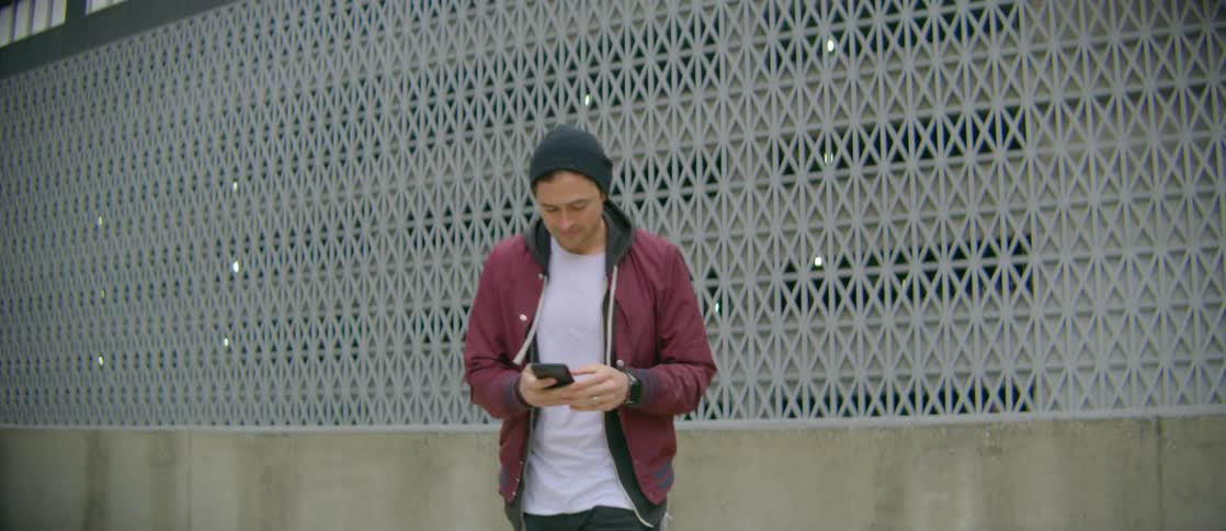 Man looks over from a building before turning to his phone