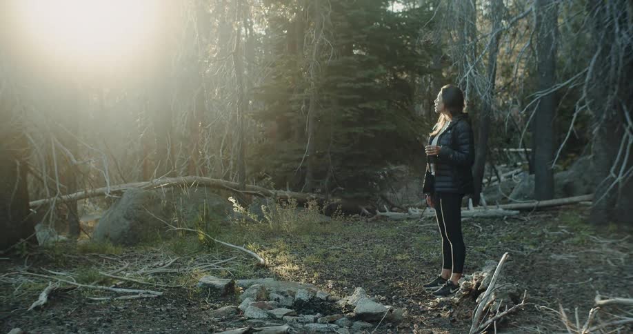 A woman standing on a clearing on the woods at sunrise