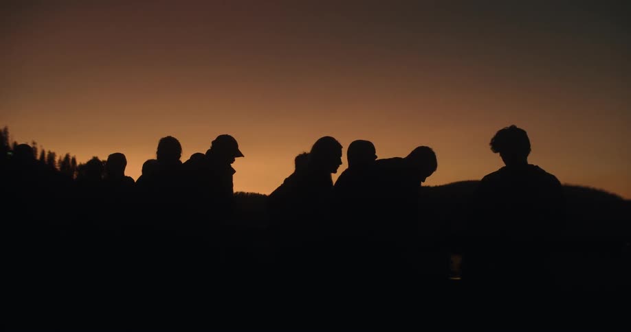 A group of people are silhouetted at dusk