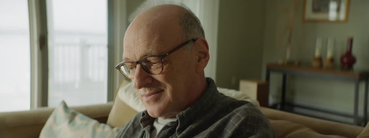 A man sits in a chair and smiles as he looks through a photo album