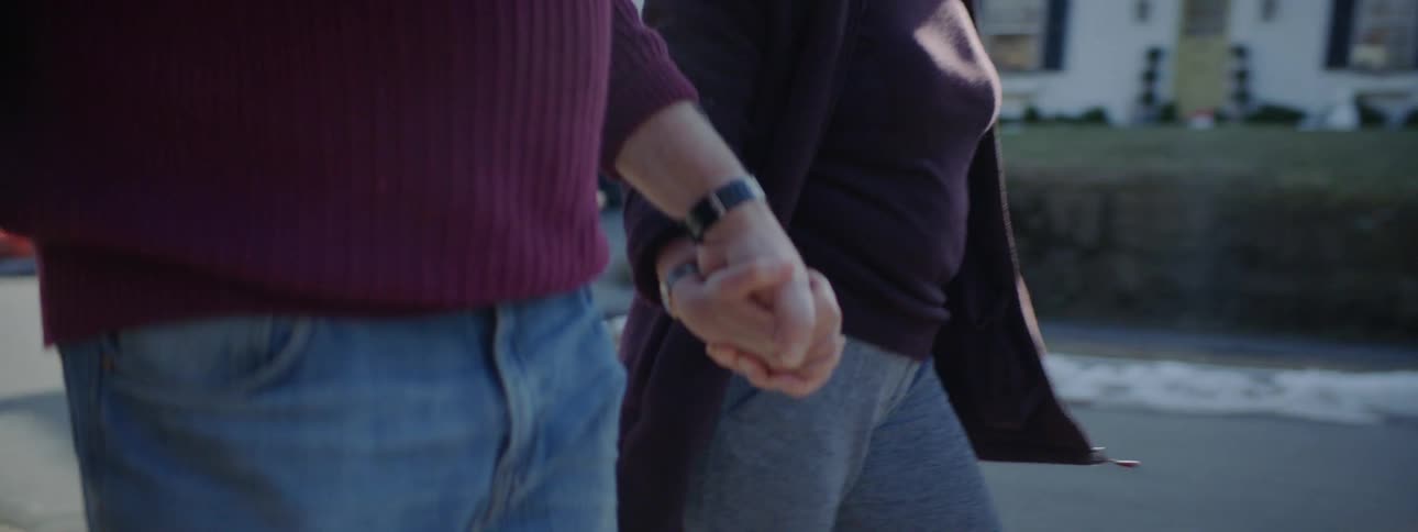 A man and a woman hold hands while walking down a sidewalk