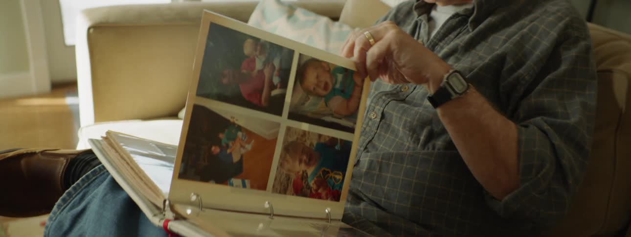An elderly man sits on a couch and looks through a photo album