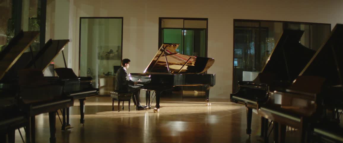 Man plays piano in hall with several pianos in it