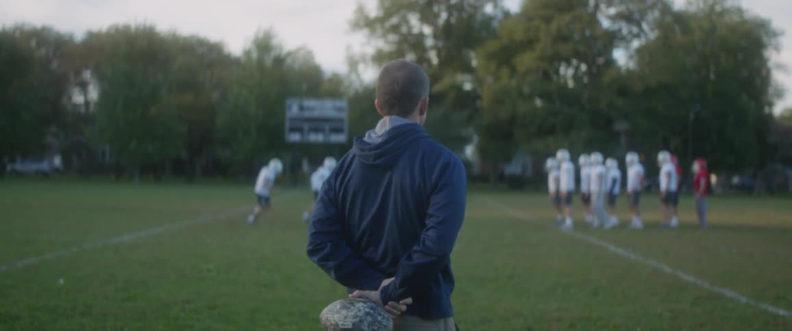 Football players on a field while the coach watches them practice