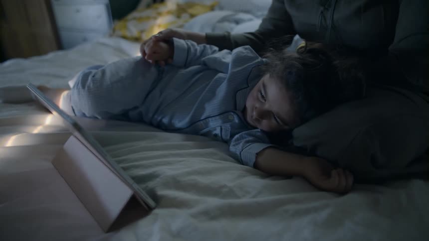 A girl and woman watching something on a tablet while laying in bed