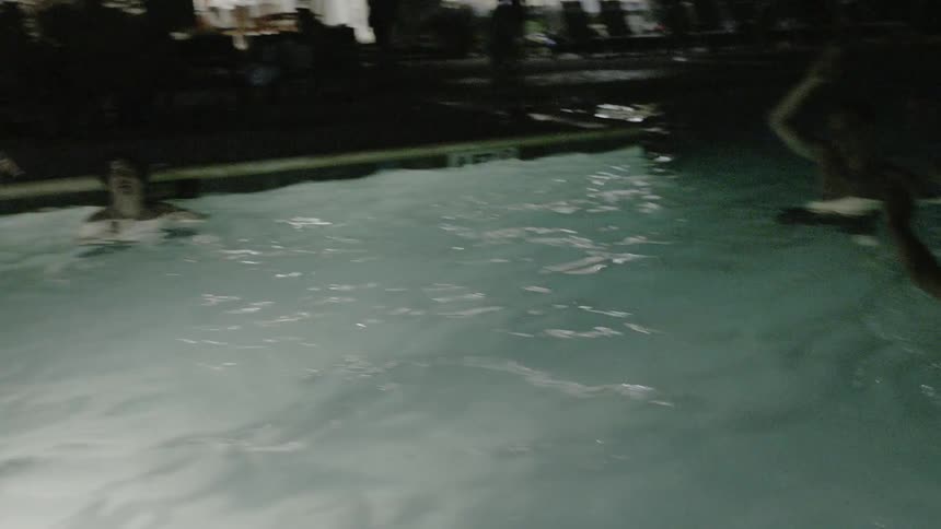 People play with a beachball in a pool at night