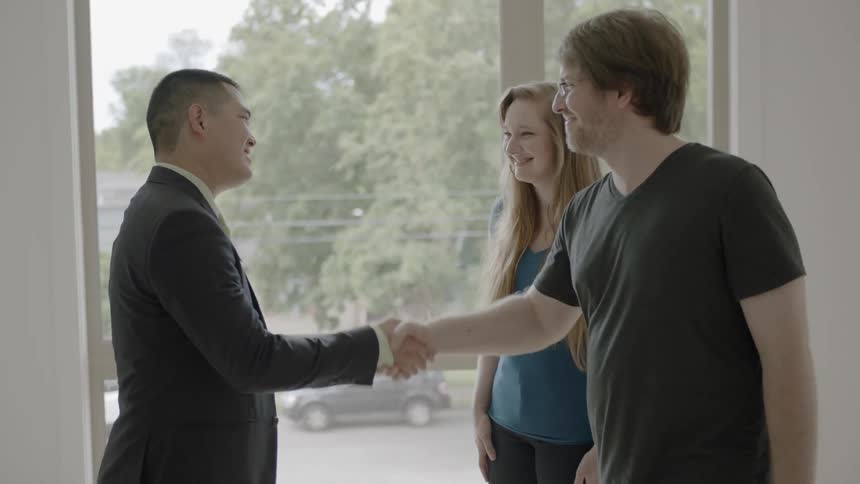 Real estate agent shakes hands of couple looking around home