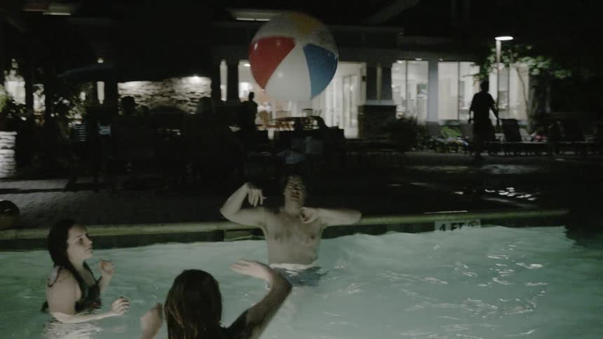 People are in a pool tossing a beach ball