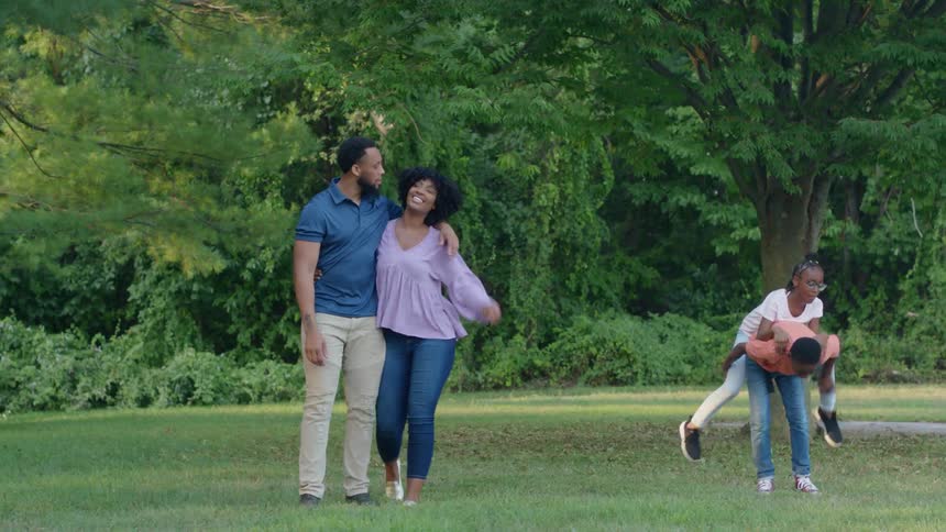 A man puts his arm around a woman while children play under a tree