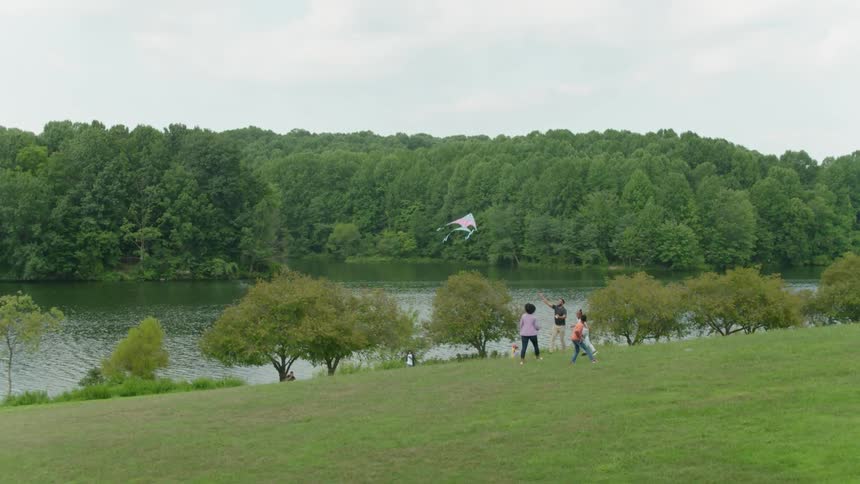 Family flies kite on hill near lake
