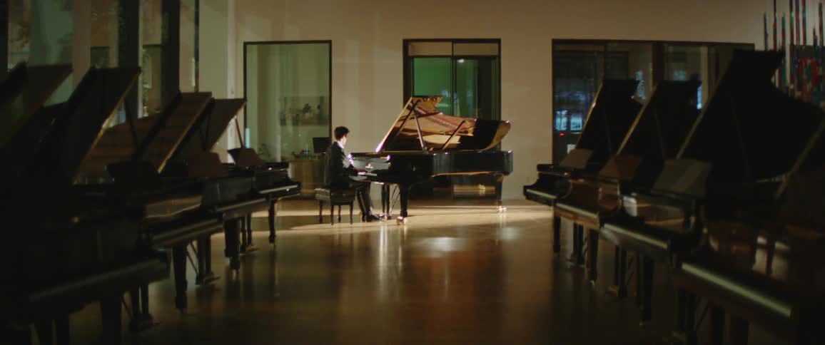 A young man in a suit plays a piano in a mostly darkened room