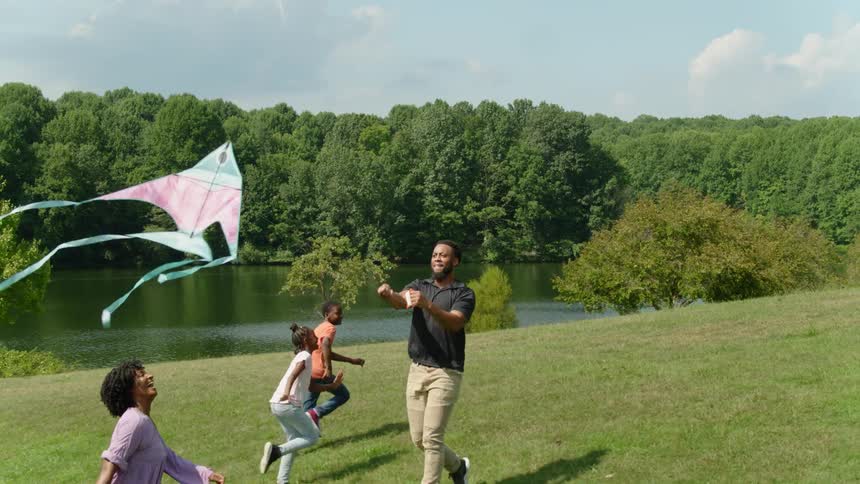 A man with his family running and flying a kite