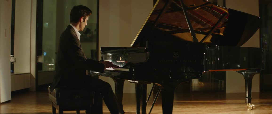 A man in a tuxedo sits at a piano and plays