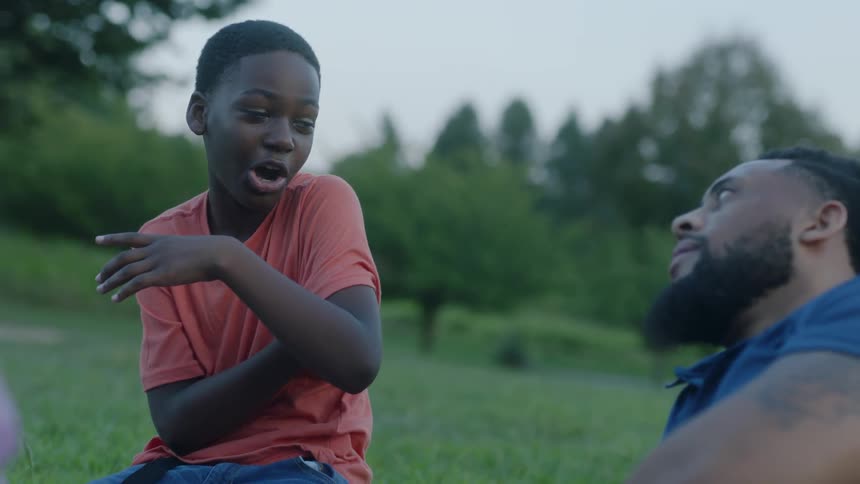 A kid telling a man a story while sitting in the grass