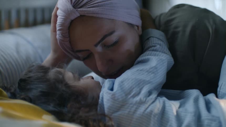 A woman playing with a little girl in bed