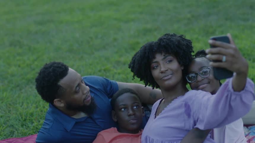 A family takes a photograph on a blanket on a grass lawn