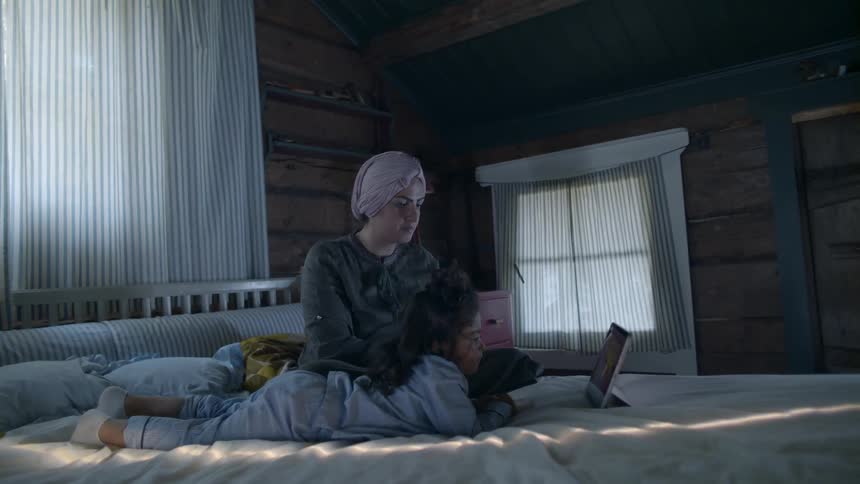 Two people in a bedroom watching something on a tablet