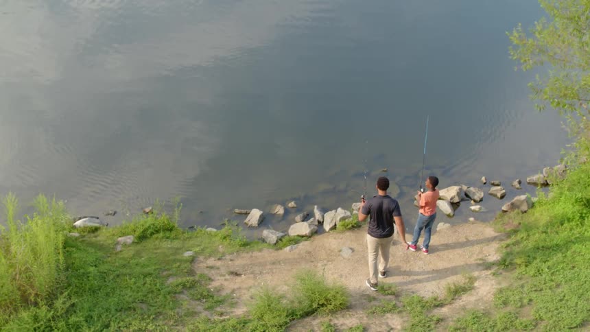Two people are fishing outside by a river