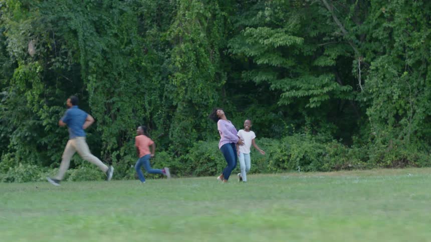 A father and son running towards a mother and daughter in a park