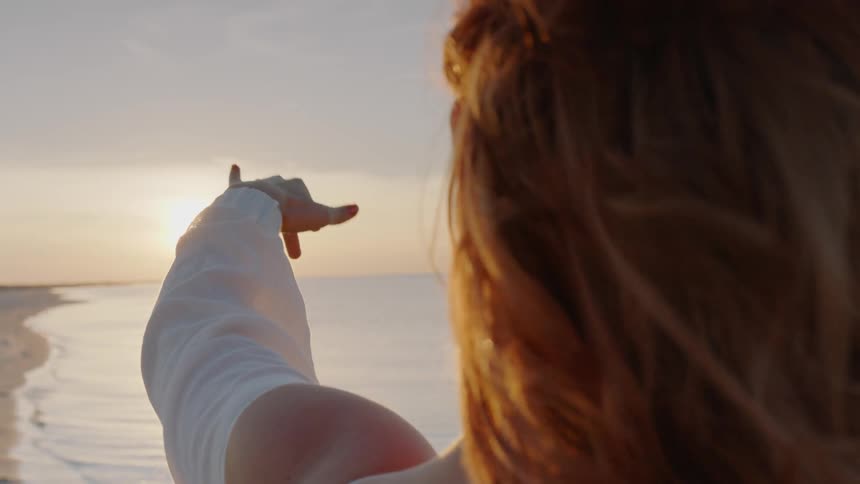 Woman stands on the beach at sunrise and reaches toward the sun
