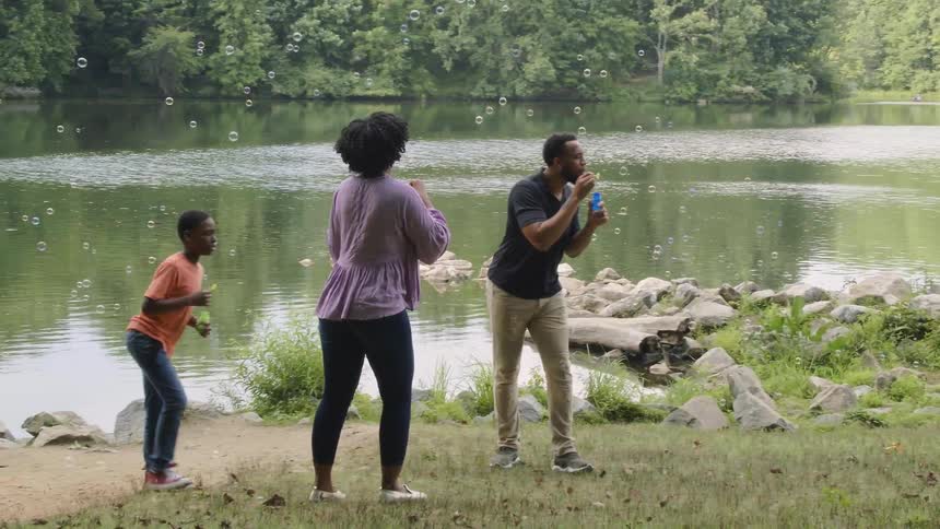 A family of four blowing bubbles near a river surrounded by trees and rocks