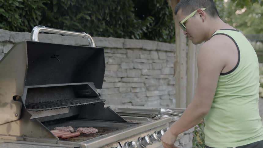 A man grills hot dogs and hamburgers on a patio