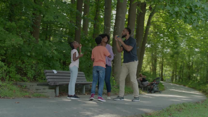 A family blow bubbles by the park bench