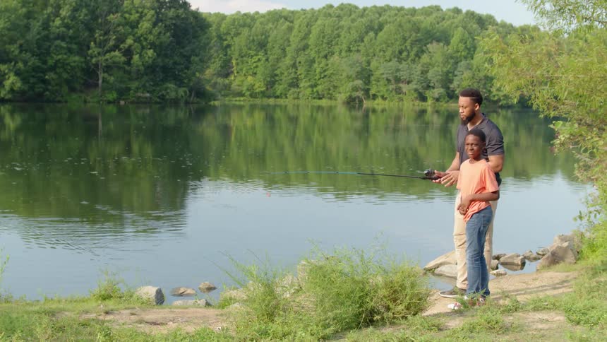 A man and boy fishing in a river at a park surrounded by trees