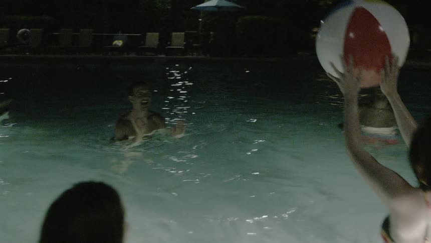 Young people playing with a beach ball in a pool at night