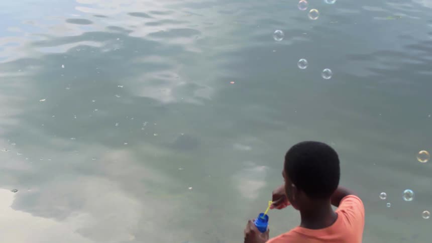 A child blowing bubbles in the air by a lake