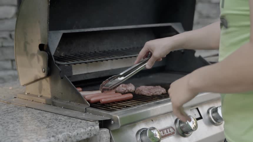 A man turning sausages on his grill