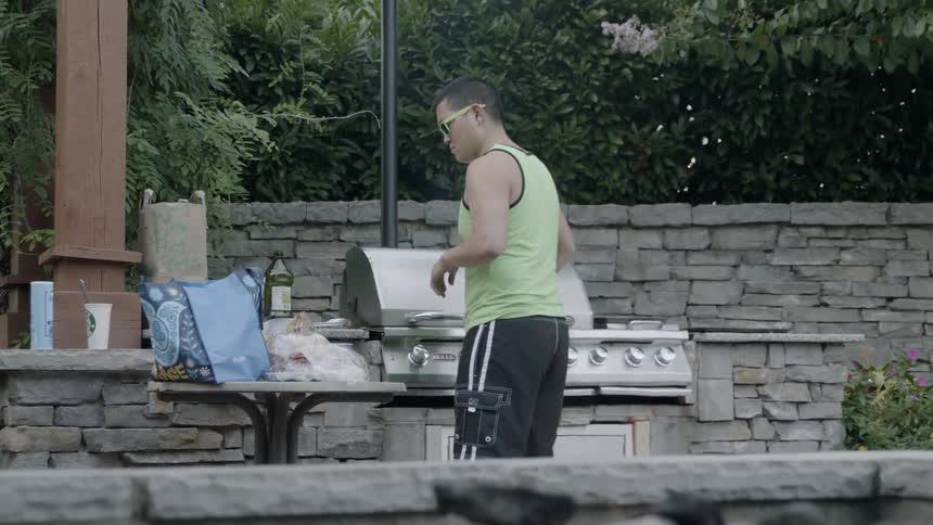 An asian man cooks food on a grill outdoors